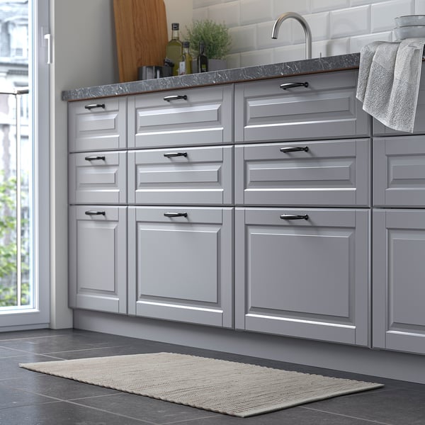 Modern kitchen with grey cabinets, sink, and a small, handwoven, beige rug on the dark floor.
