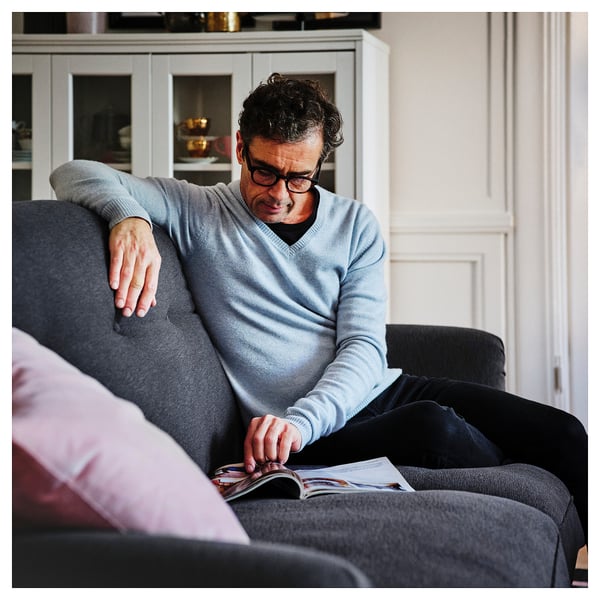 Person in light blue sweater reading magazine on soft grey ESSEBODA sofa, relaxed at home.