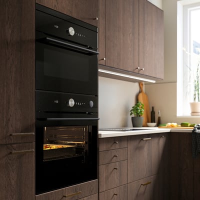 Modern kitchen with double black ovens, wooden cabinets, a white countertop, and a window.