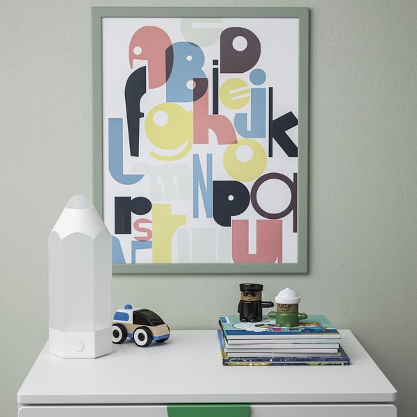 Kids wall frame with colourful letters hangs above shelf with car, lamp, books. Safe, plastic front.