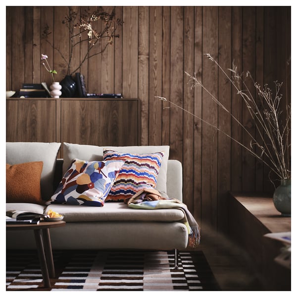 Cosy living room with grey couch, colourful pillows, striped blanket, patterned rug, and vase with branches.