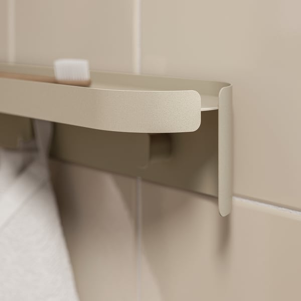 A beige metal shelving unit with three hooks mounted on a beige wall. The hooks hold two toothbrushes.