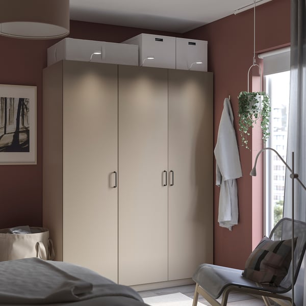 Modern closet with beige doors and white boxes, located near a window with a hanging plant and a chair.