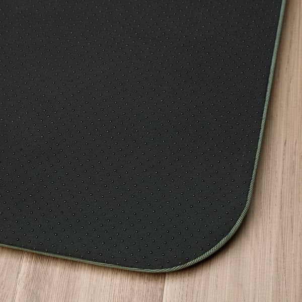 Black antibacterial standing mat with textured surface and green edge, laid on wooden floor.