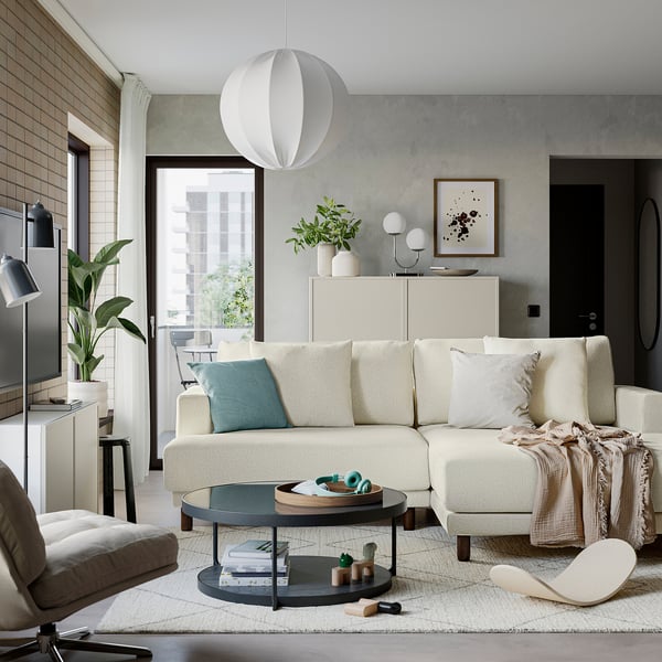 Modern living room with white sofa, black coffee table, and large window. Decorative plants and unique lighting.
