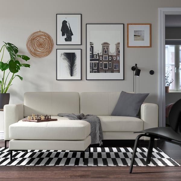 Modern living room with sofa, chess set, rug, art wall, lamp, plant.