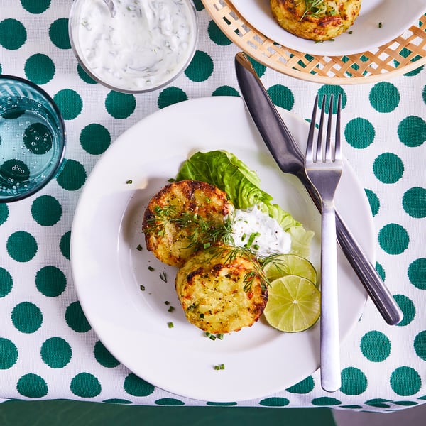 Two golden-brown cakes on a white plate with lettuce, lime, fork, knife, and sauce.