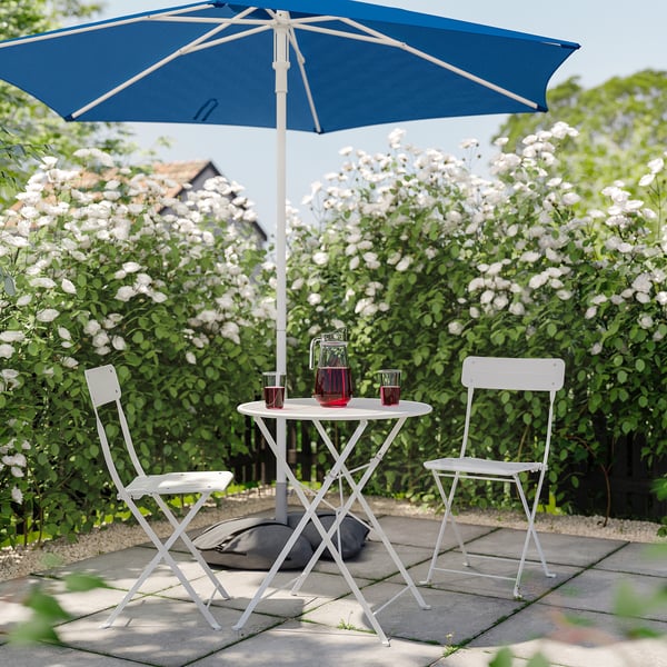 Garden with white table, chairs, blue parasol, and white flowers.