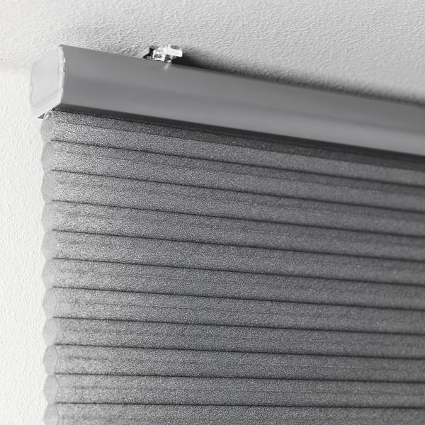 Close-up of a partially rolled-up, cellular honeycomb-insulated window blind, attached along a white ceiling, offering room darkening and privacy.