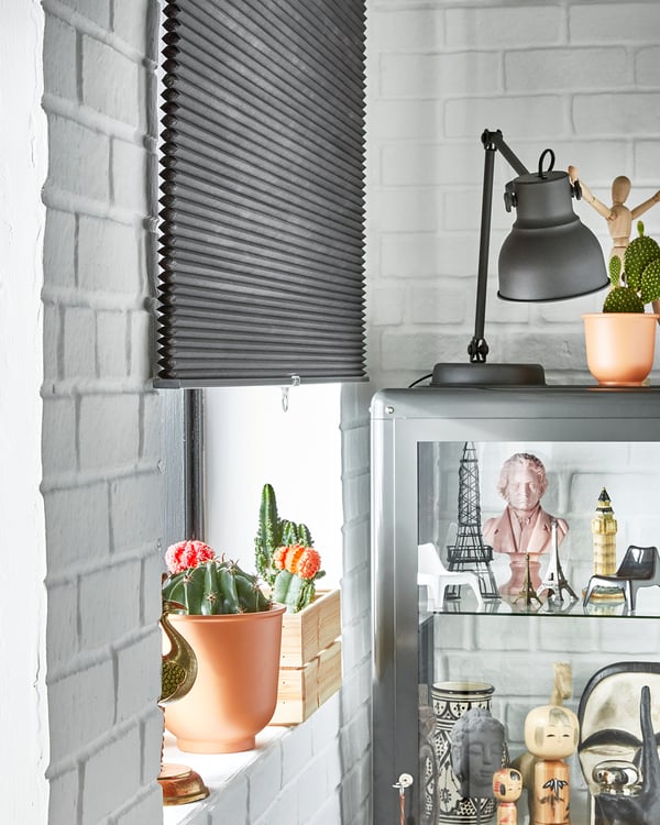 Modern room with white brick walls, gray blinds, and various decor items including cacti, dolls, and a lamp.