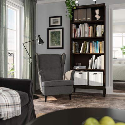 Cosy reading nook with grey IDANÄS bookshelf, black chair, lamp, and framed art on grey walls.