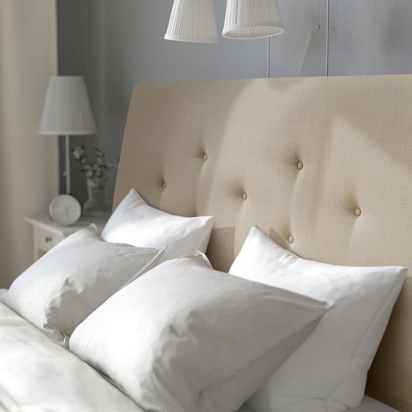Large, cosy bed with beige headboard, white pillows, sheets, sides, and lamps.