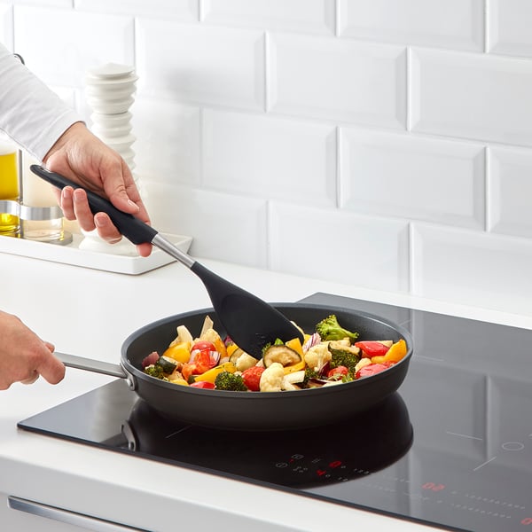 Cooking colourful veggies in frying pan with spatula, induction stove.