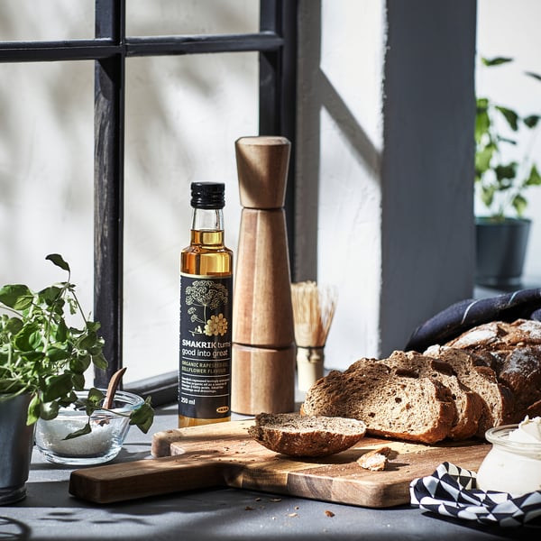 Wooden pepper grinder near kitchen window with bread and plants.