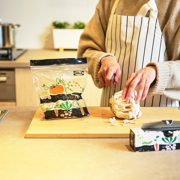 Person slicing garlic with knife on cutting board. IKEA ISTAD reusable bag nearby.