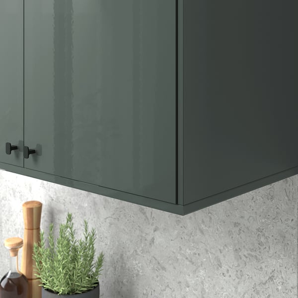 Gray-green glossy cabinet with black handle above textured grey backsplash, hiding cords and lighting under.