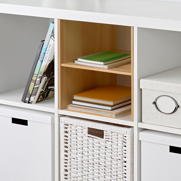 White shelves with KALLAX pine inserts holding colourful books and a white basket.