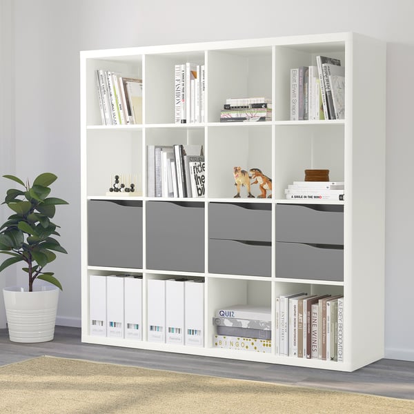 White KALLAX bookshelf with books, bins, and plant. Offers versatile storage for books, magazines, and decor.