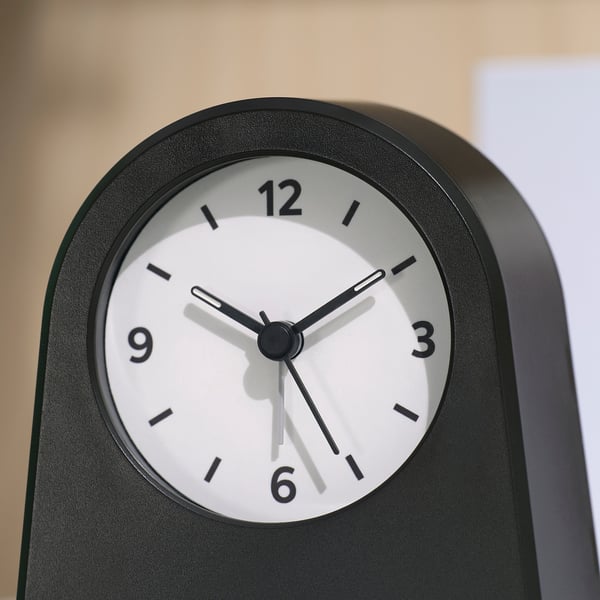 Modern, black alarm clock with white face, bold black numbers, and luminous hands, showing time 10:10.