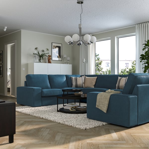 Modern living room with blue KIVIK sofa, chaise lounge, chandelier, coffee table, rug, and green walls.