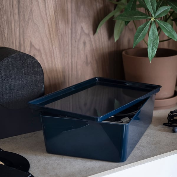 A blue KUGGIS box sits on a desk, storing items neatly. The box, with its glossy finish, is ideal for organising desk accessories or media gadgets.