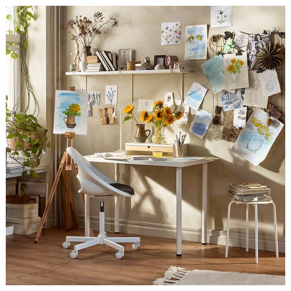 Artists studio with white LAGKAPTEN desk, flowers, paintings, and plants.