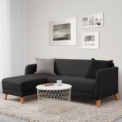 Modern living room: l-shaped black LINANÄS sofa, grey pillows, white round coffee table beneath wall art on light wall. Cosy, compact.