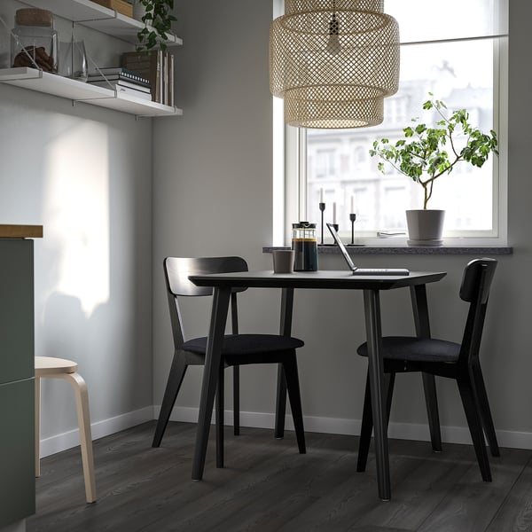 Modern dining set with dark table and chairs, padded seats, under window with laptop and plant.