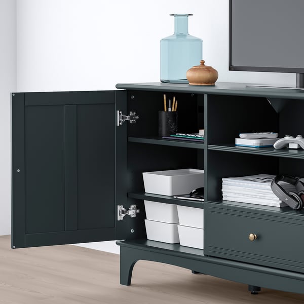 Dark green LOMMARP tv stand with open door revealing storage compartments and organisation solutions, including a drawer and stacks of white boxes.
