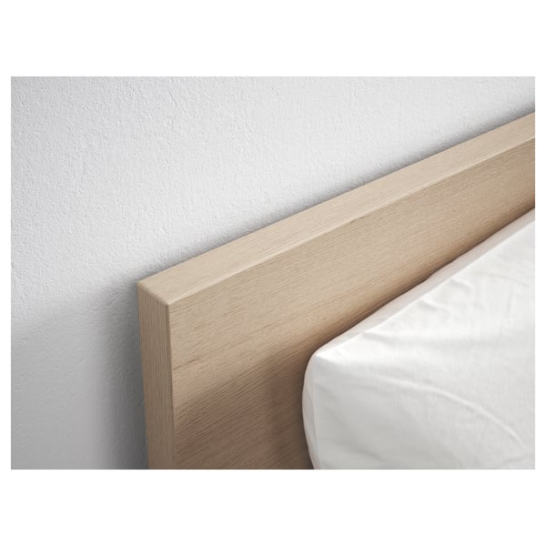 A close-up of a light oak wood headboard against a white wall, part of the MALM bed frame.