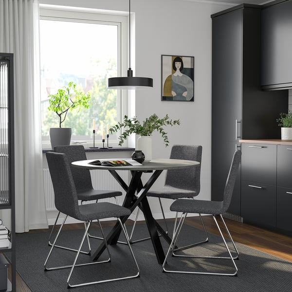 Modern dining set with round table and grey chairs, sleek legs, polyester upholstery, cosy kitchen corner with art and plants.