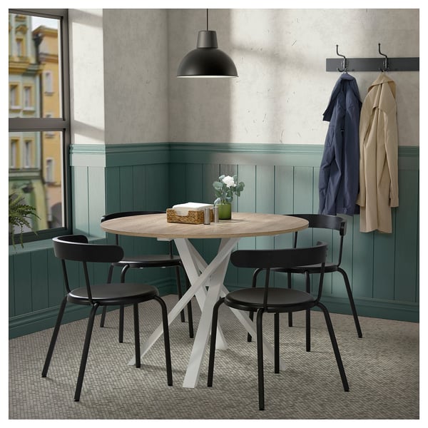 Modern dining set with round table, white frame, black chairs. Cosy corner with green wall and coat hooks.