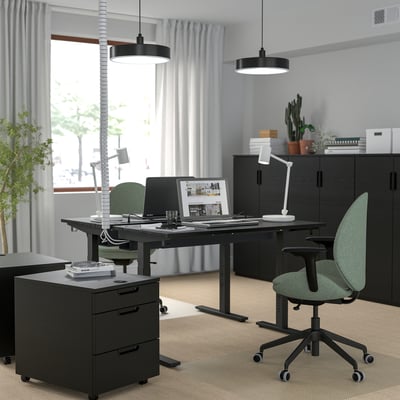 Home office setup featuring MITTZON black height-adjustable desk, green chairs, and black cabinets, with a large window and hanging lights.
