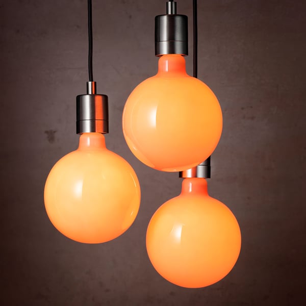 Three round, orange light bulbs hang from black cables against a dark wall. Each bulb has a warm, candle-like glow and emits a cosy light.