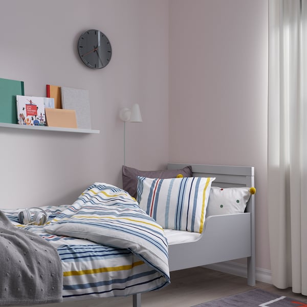 A tidy bedroom with NATTSLÄNDA blue/yellow striped duvet, white bed, soft cotton, and bookshelf.