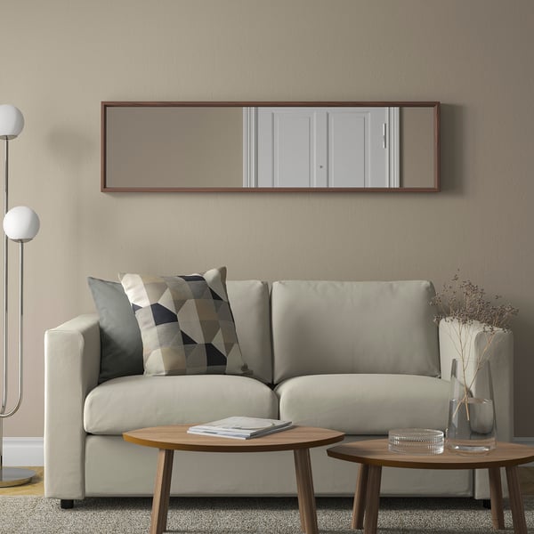 Small living room with large mirror, light grey sofa, round wooden tables, floor lamp, and decorative vase.