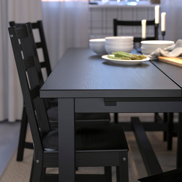 Modern black dining set with extendable table and matching chairs, white dishes, and green vegetables on table.