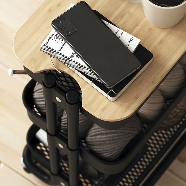 A smartphone on a bamboo lid atop a trolley, hiding clutter.