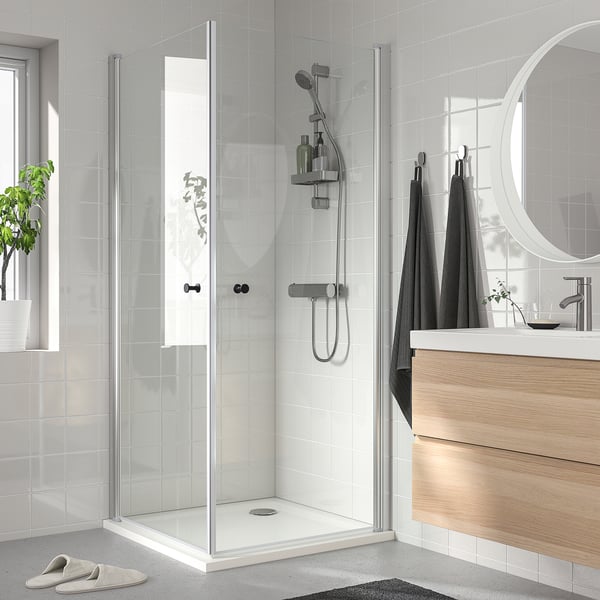 Modern minimalist shower with glass doors, silver fixtures, and built-in shelf. Dark towels and slippers nearby.