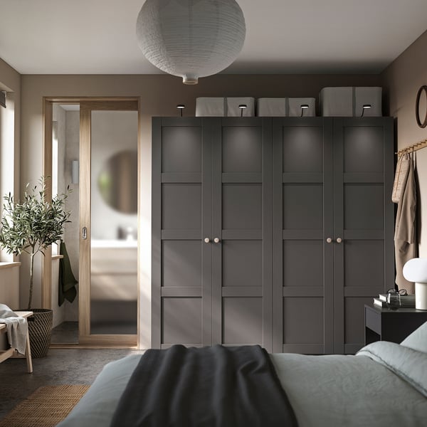 Modern bedroom with black PAX wardrobe, grey handles, and top storage. Cosy bed with blue blanket, lantern light, and green plant.