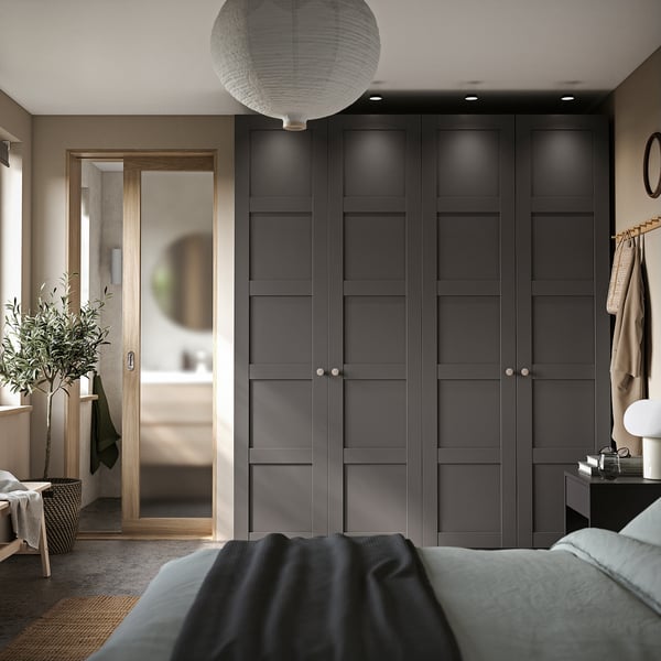 Modern bedroom with black wardrobe, wood accents, hanging plants, blue bed, grey rug, and round light.