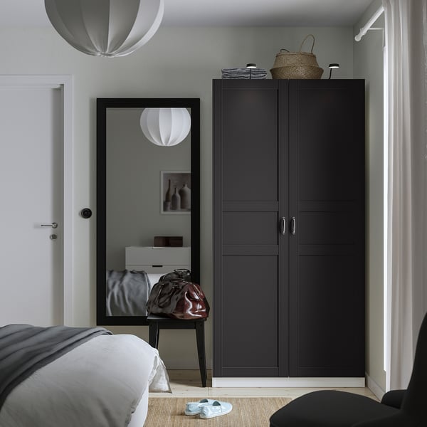 Modern bedroom with black PAX wardrobe, mirror, bed, and baskets. White pendant lights, grey rug, and sandals.
