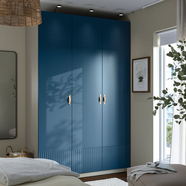 A tall blue PAX wardrobe with gold handles and mirror, next to a bed and window.