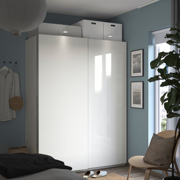 Minimalist bedroom with white PAX wardrobe, blue walls, grey decor, plant, photos, and wooden chair.
