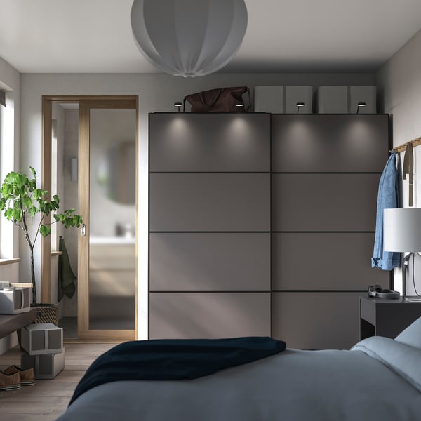 Modern bedroom with black PAX wardrobe, sliding doors, grey bed, white lamp, and plant.