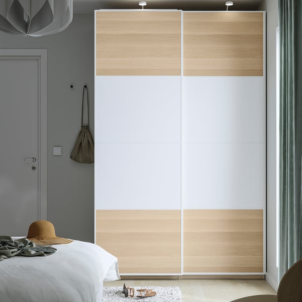 Minimalist bedroom with PAX closet, light wood, white sliding doors. Bed, small rug, beige hat, bag.
