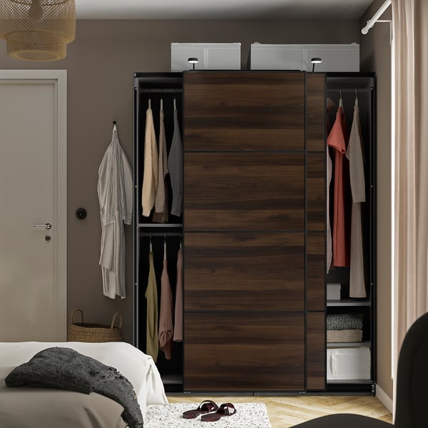 Wooden sliding closet with hanging clothes; next to bed with blanket and flip-flops.