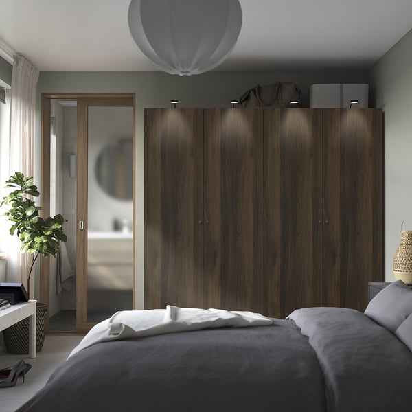 Modern bedroom large dark wood PAX wardrobe with sleek handles, housing bags atop, flanked by curtains. A grey bed with white linens is in foreground.