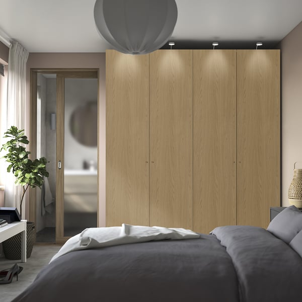 Modern bedroom with PAX wardrobe, bed, and plant. Wardrobe dominant, light wood, subtle lighting.
