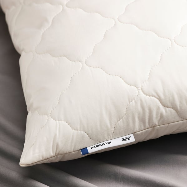 Close-up of a soft, white pillow with a tag reading RÅDHUSVIN and ikea logo. Pillow has a diamond quilt pattern and a cotton exterior.